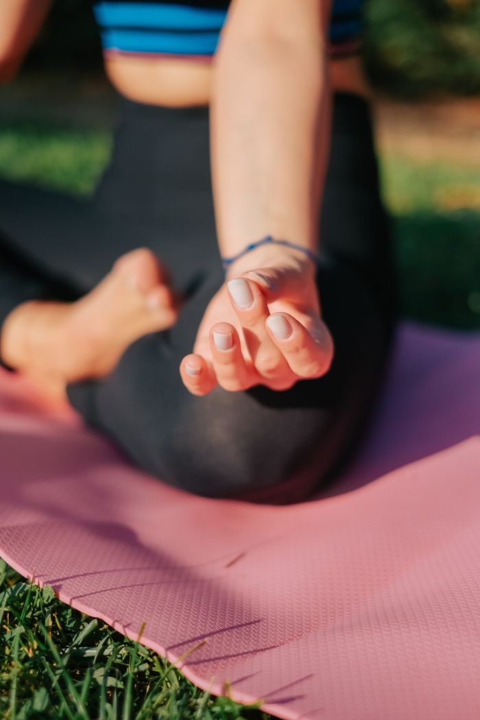 services-03 Close-up of a woman meditating in the lotus position on a pink yoga mat outdoors.