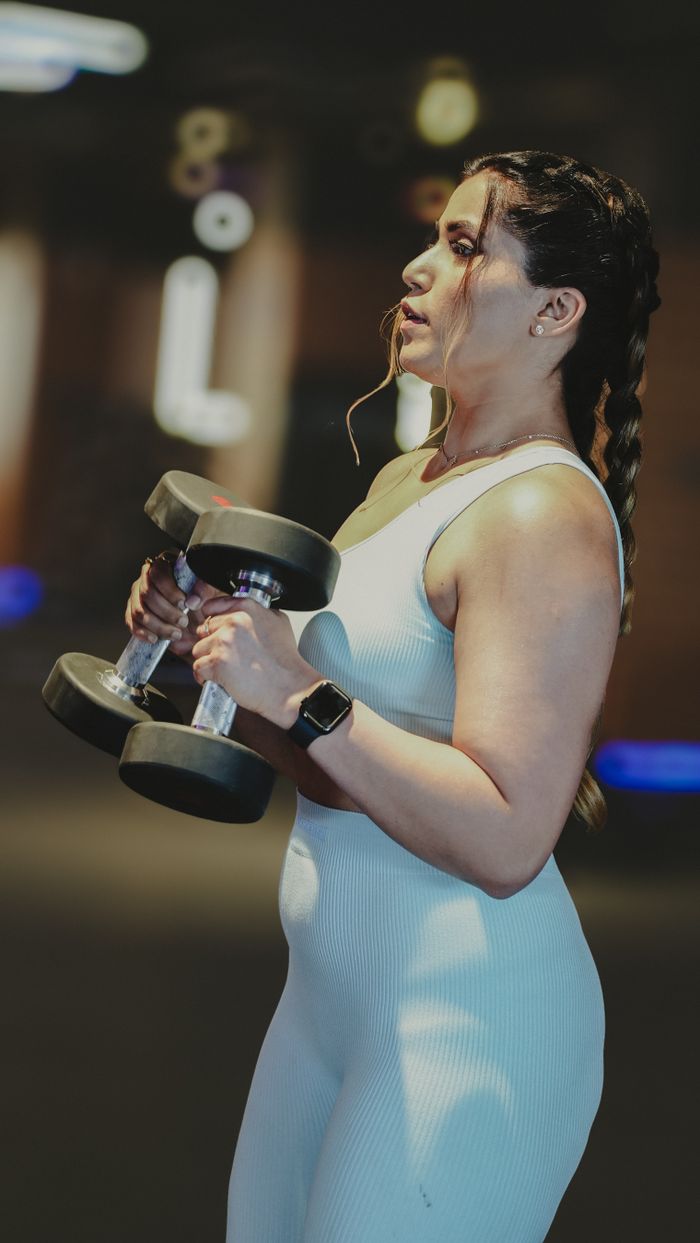 services-img A focused woman lifting dumbbells during a workout in a gym, showcasing strength and fitness.